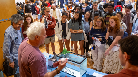 Group of UNC-Chapel Hill students at a research fair attending a demonstration by two professors who conduct fluid research.